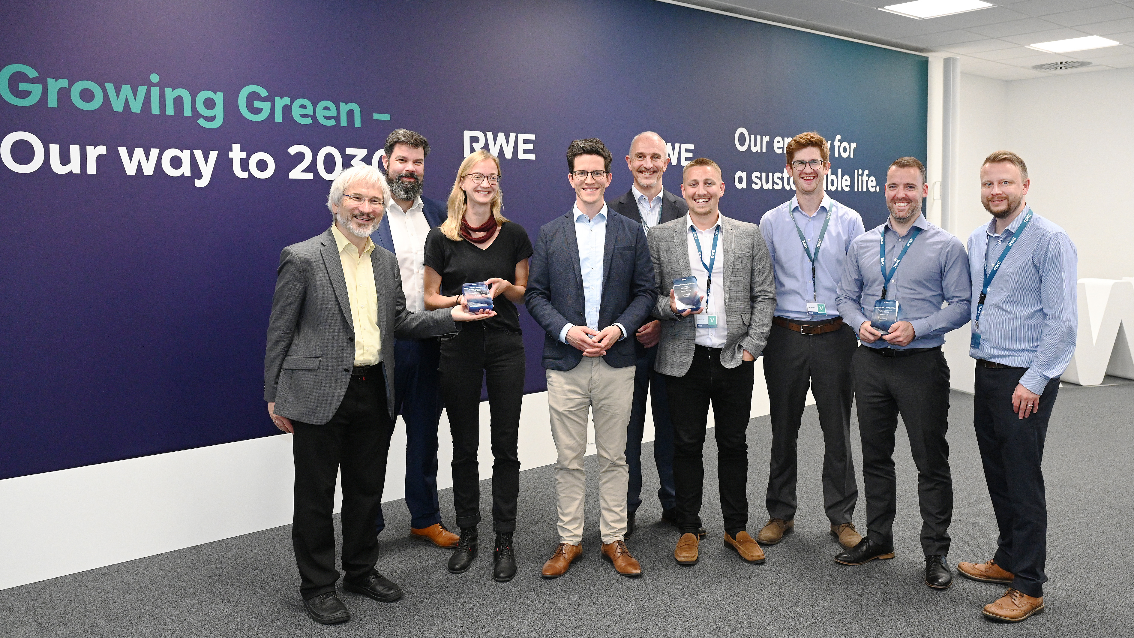 A group of professionals standing together, holding awards, in front of a 'Growing Green' wall banner.