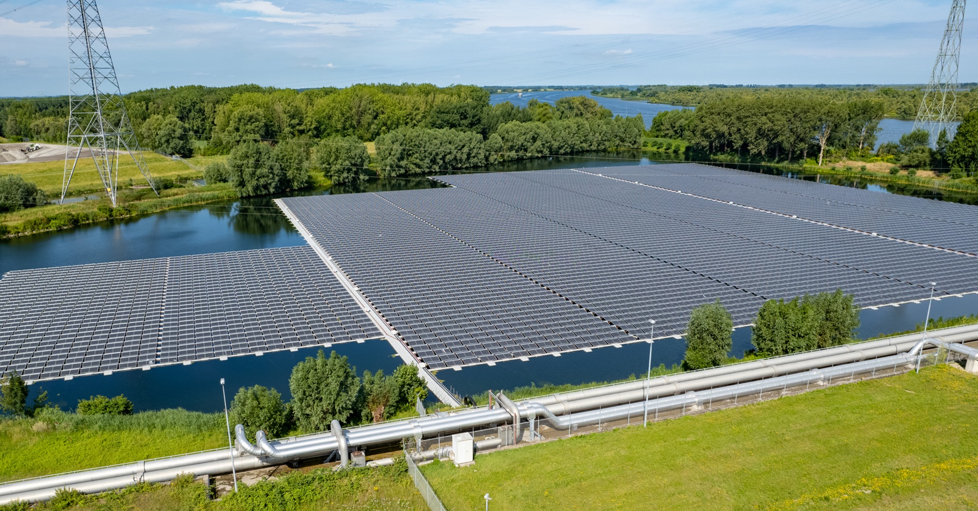 Een groot zonnepaneel ligt op water, omringd door groene bomen en een elektriciteitslijn in de verte.