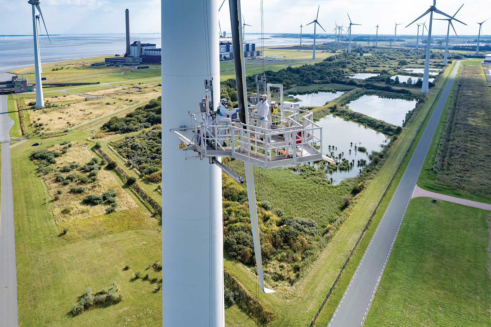 Een windturbine die vanaf een platform wordt onderhouden. Op de achtergrond staan andere turbines en groene landschappen.