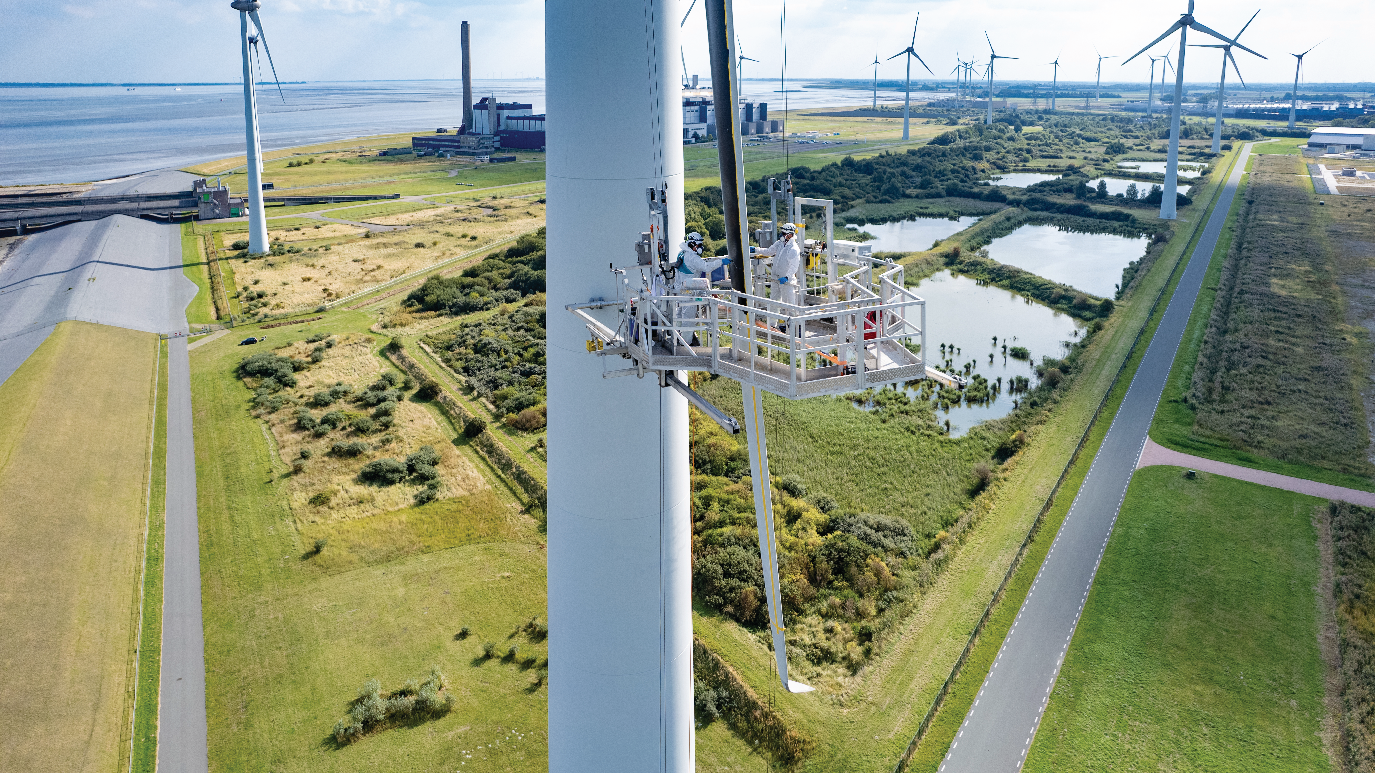 Een windturbine die vanaf een platform wordt onderhouden. Op de achtergrond staan andere turbines en groene landschappen.
