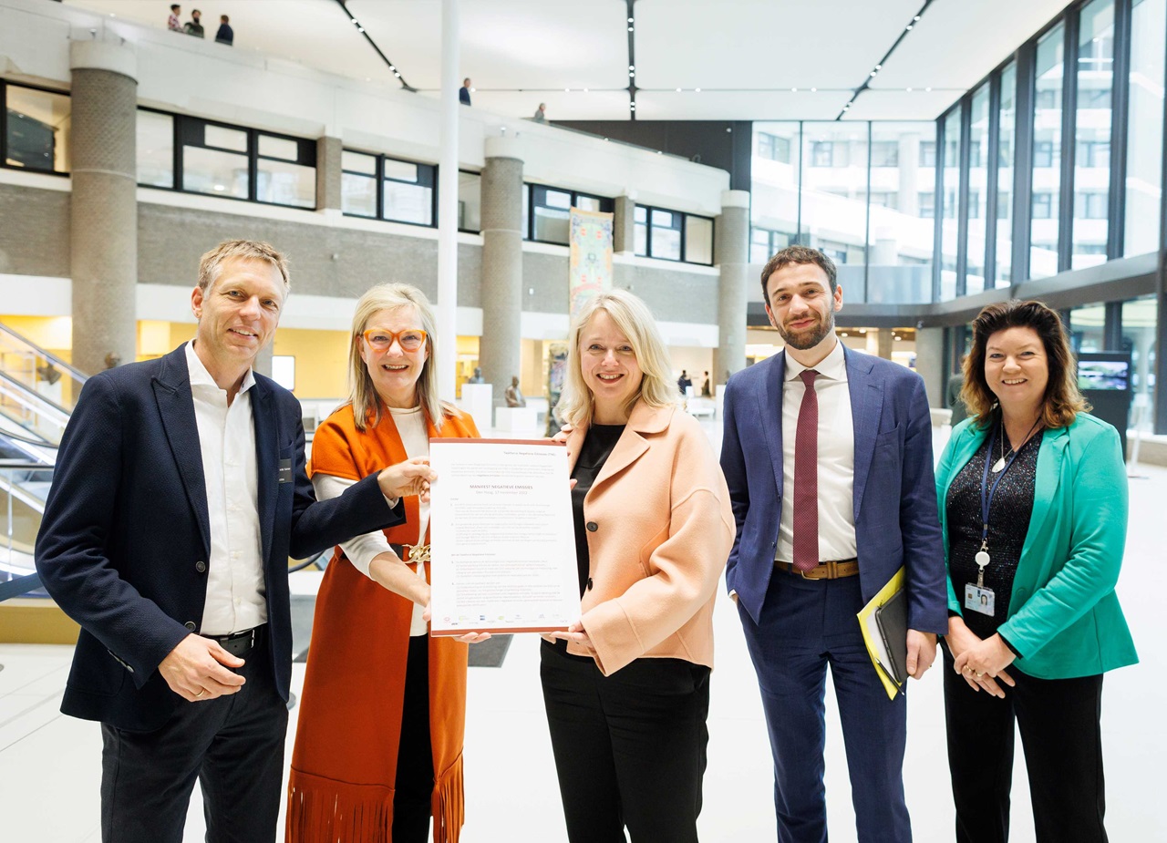 Een groep professionals houdt een document vast in een modern gebouw met grote ramen en een open indeling.