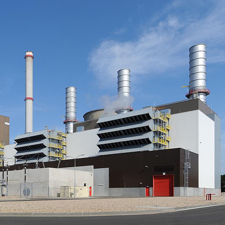 A modern power plant featuring multiple tall chimneys, metallic structures, and a red door under a clear blue sky.