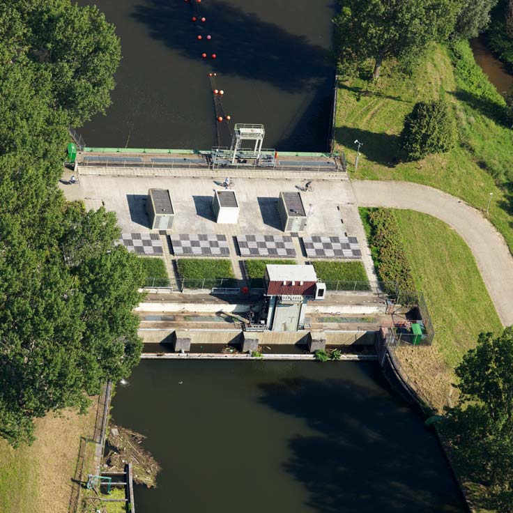 Aerial view of a water management facility with control structures, checkered patterns, and surrounding greenery.