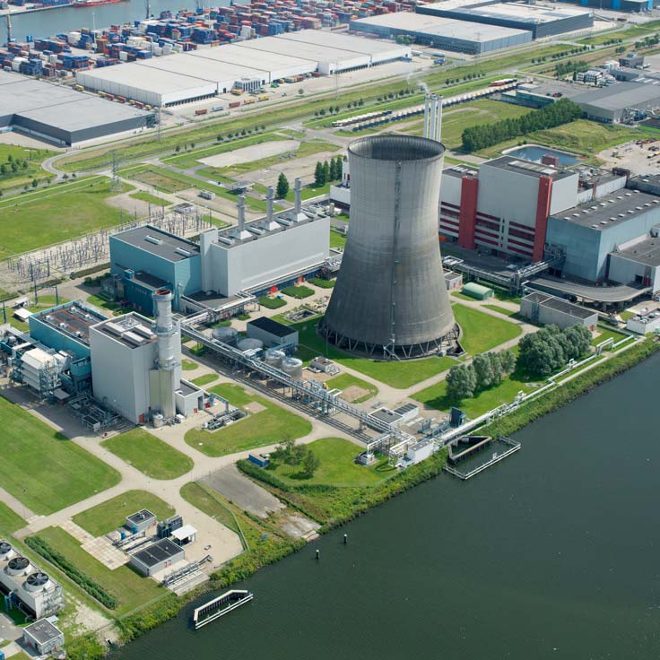 Aerial view of an industrial complex featuring a cooling tower, power plants, and containers by a waterway.