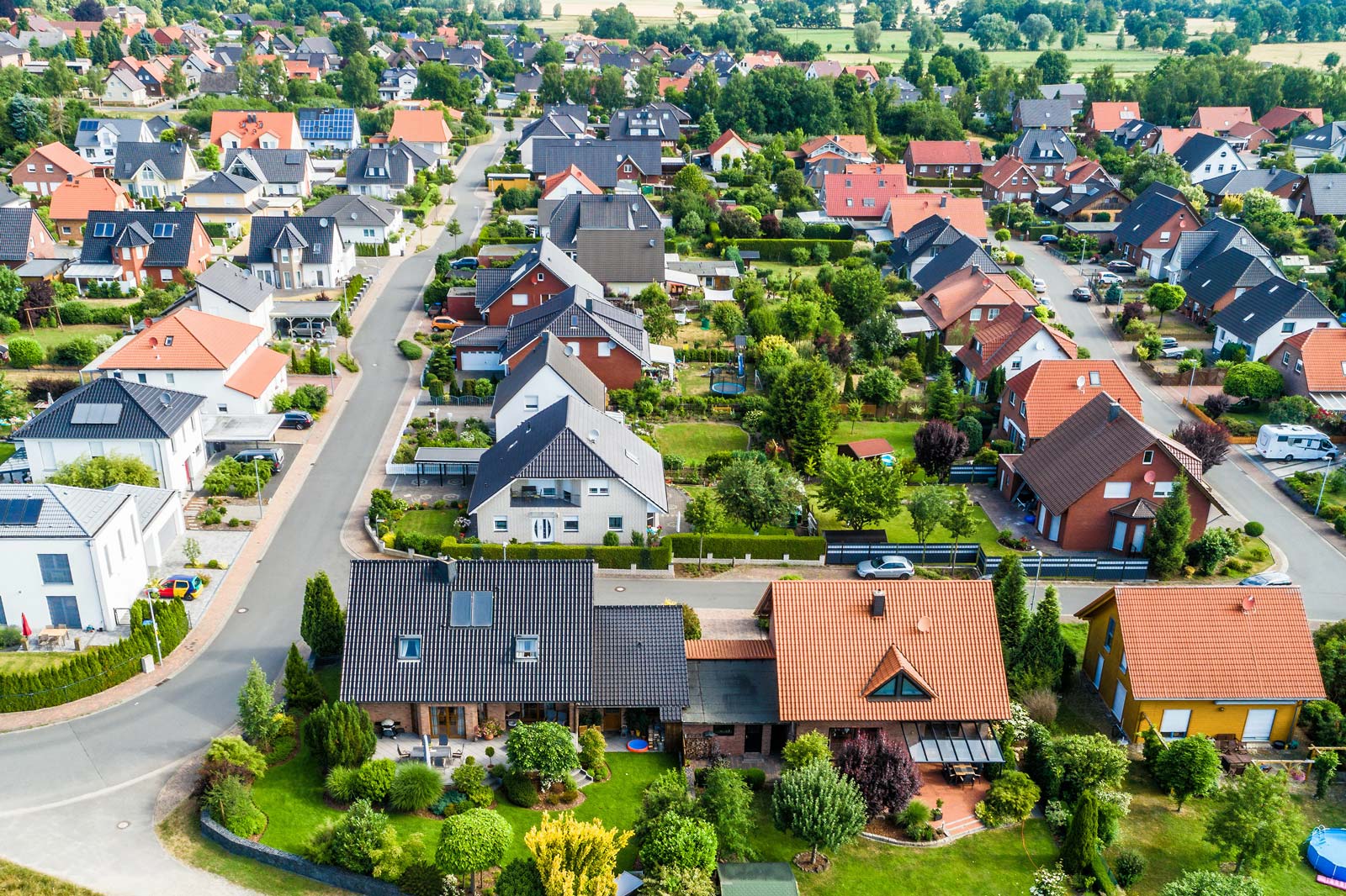 Luchtfoto van een woonwijk met verschillende huizen en groene tuinen. De daken zijn kleurig en de straten zijn met bomen omzoomd.