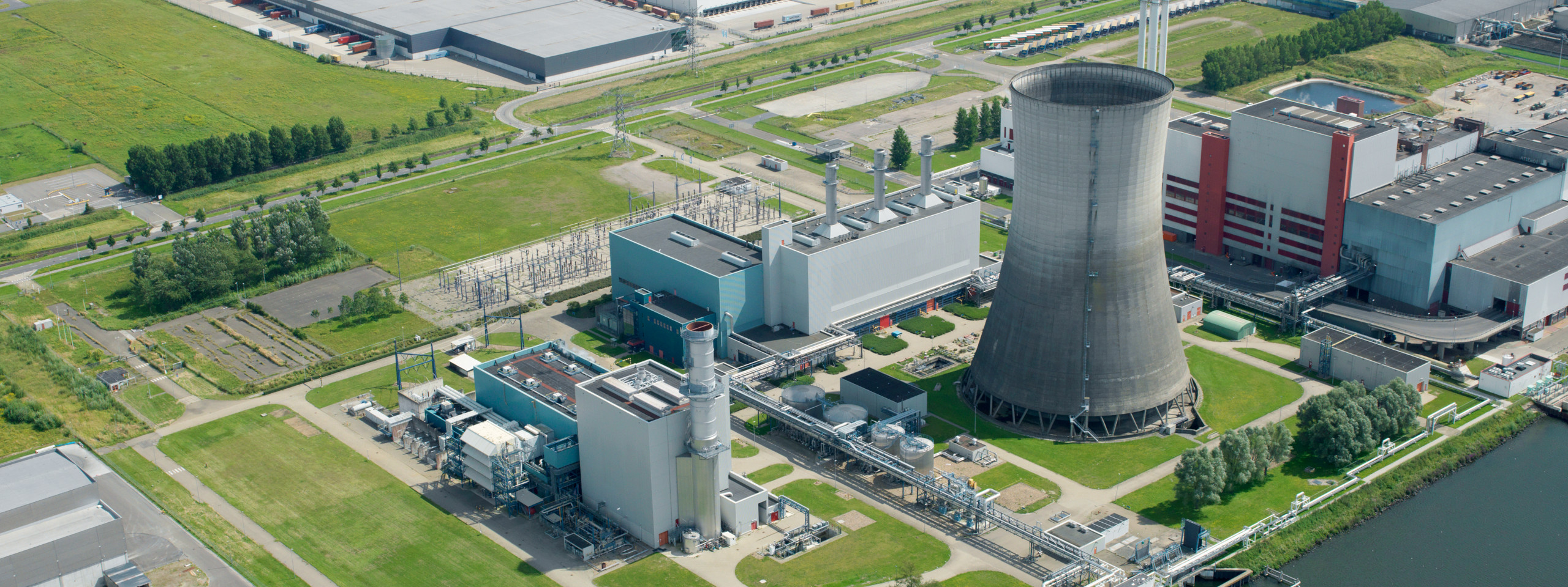 Aerial view of an industrial complex featuring a cooling tower, several buildings, and green areas.