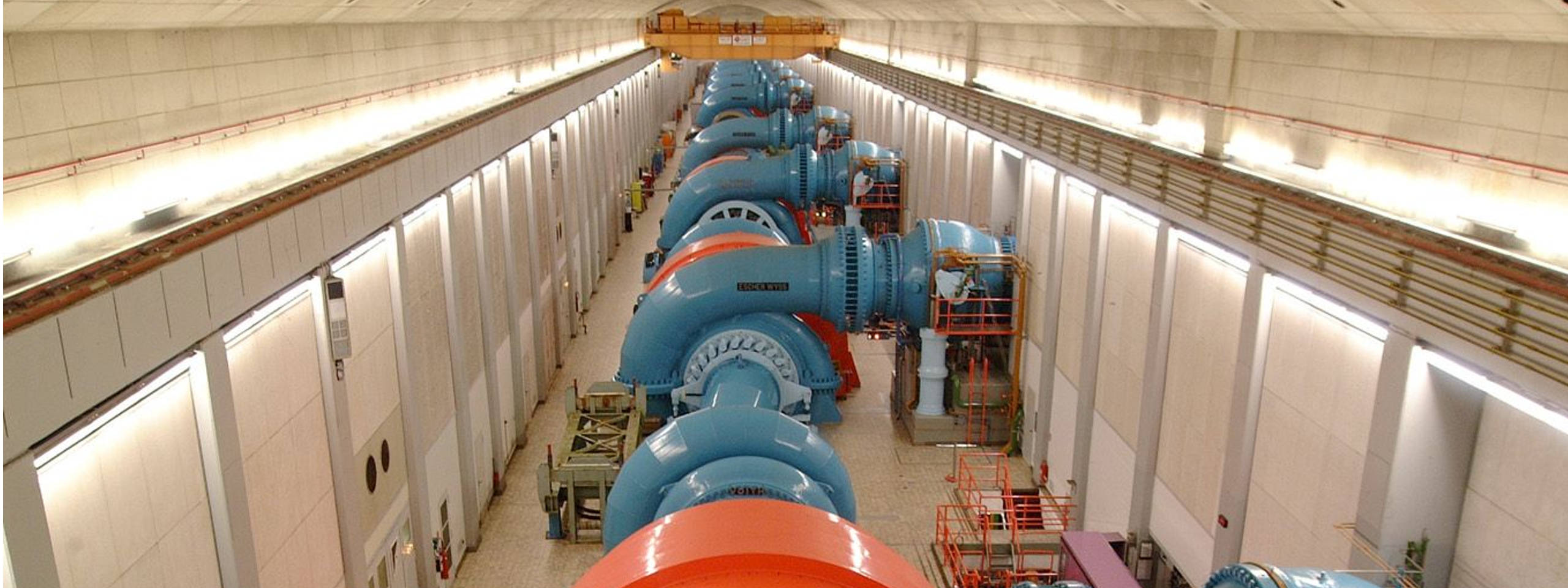 A row of blue turbines in a large room with bright lights and orange details.