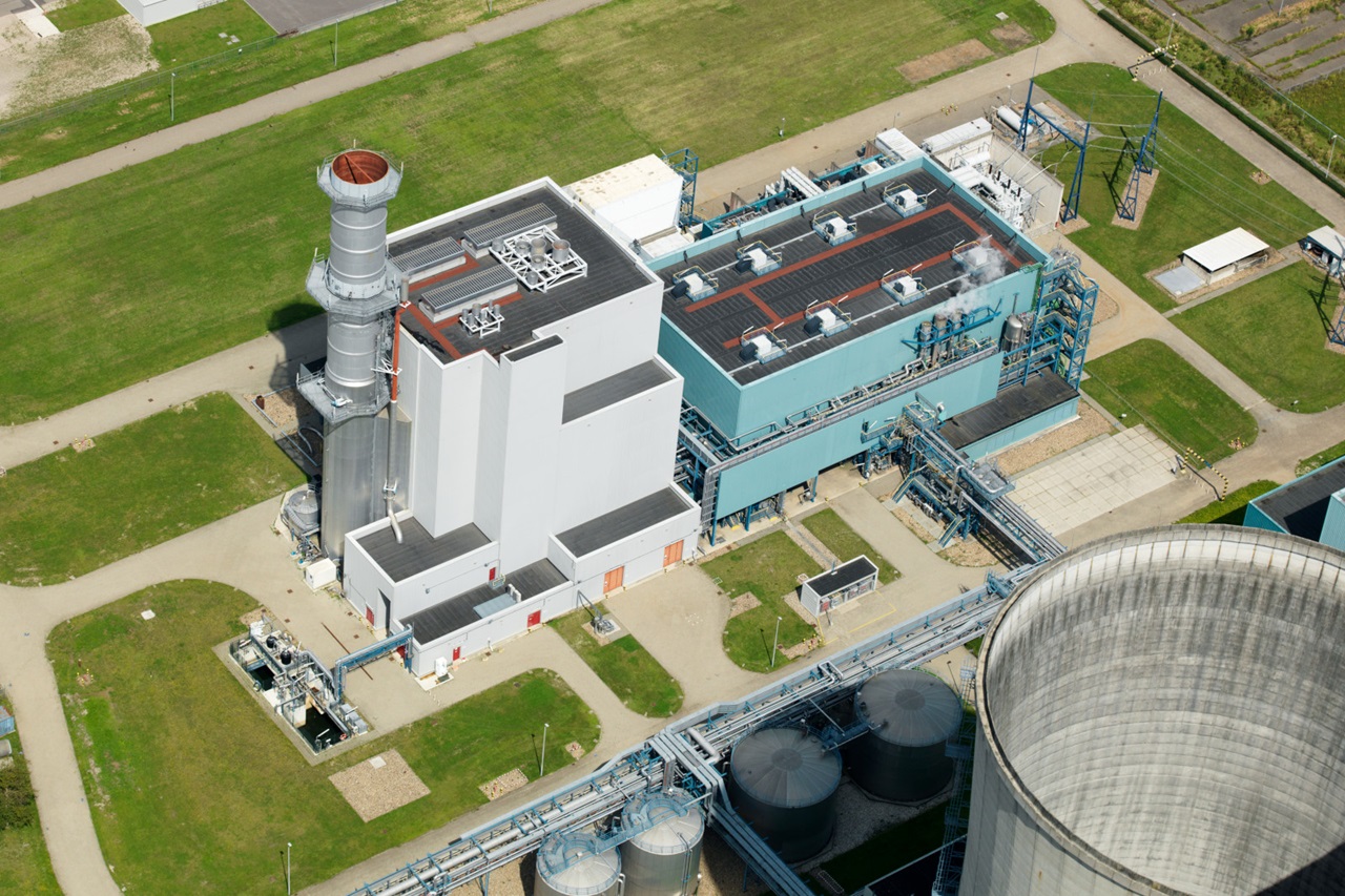 Aerial view of a power plant featuring smokestacks, large buildings, and green surrounding areas.