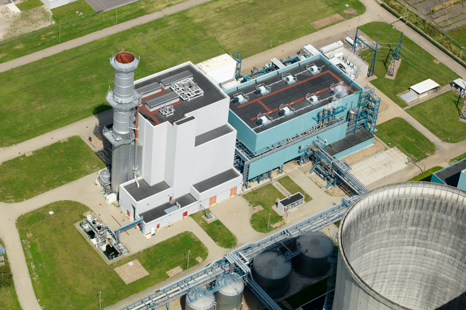 Luchtfoto van een energiecentrale met schoorstenen, grote gebouwen en groene omliggende gebieden.