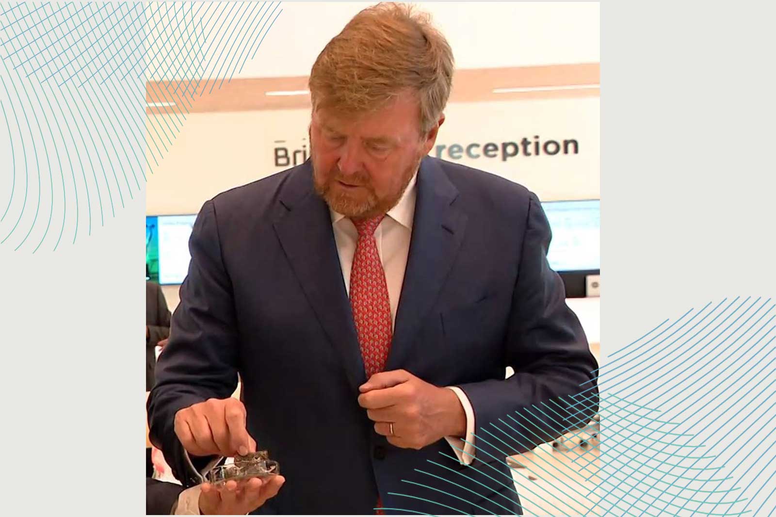 Een man in een donker pak houdt een klein voorwerp in zijn handen, staande in een helder verlichte receptie.