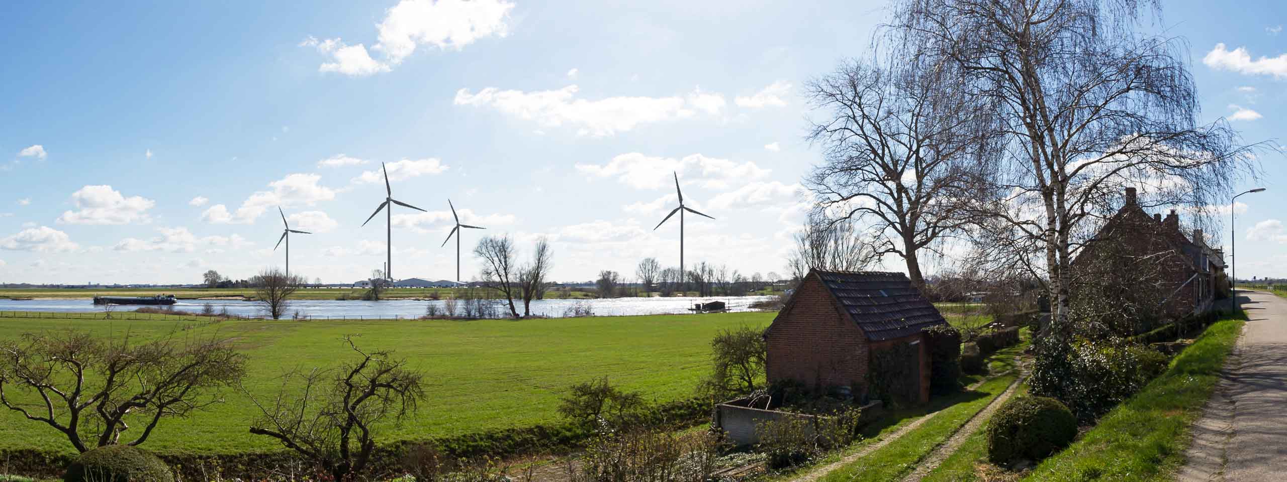 A scenic landscape featuring wind turbines, lush green fields, and a calm river under a bright blue sky with fluffy clouds.