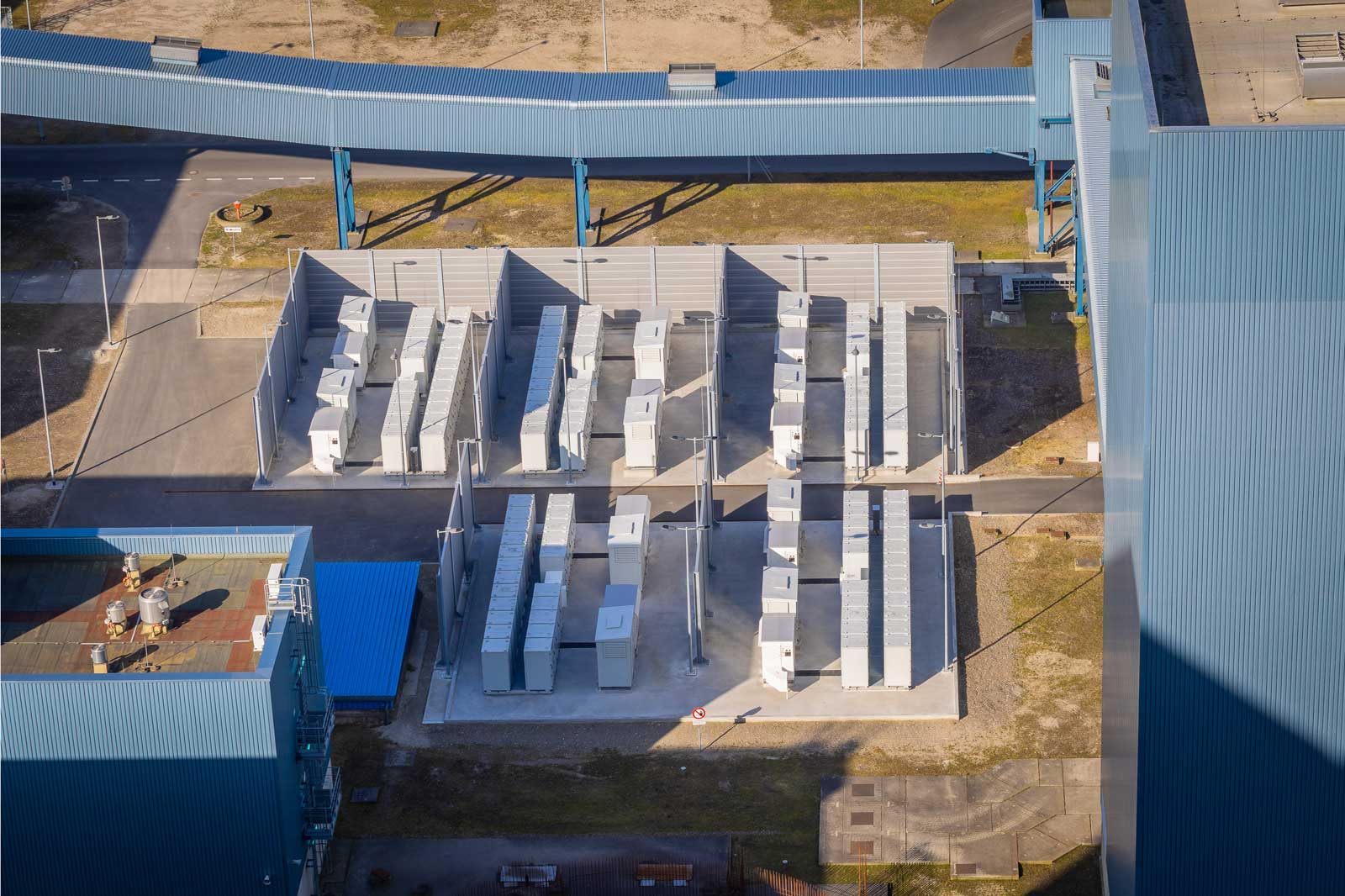 Een luchtfoto van een faciliteit met verschillende rijen witte containers omringd door grijze muren en blauwe structuren.