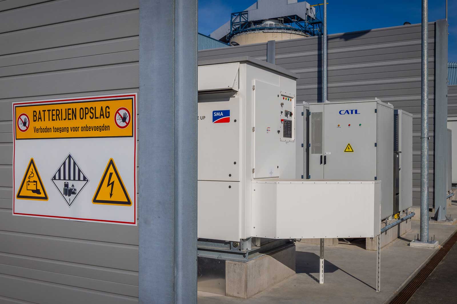Een industriële batterijopslagruimte met waarschuwingsborden tegen onbevoegde toegang, naast batterijbeheersystemen.