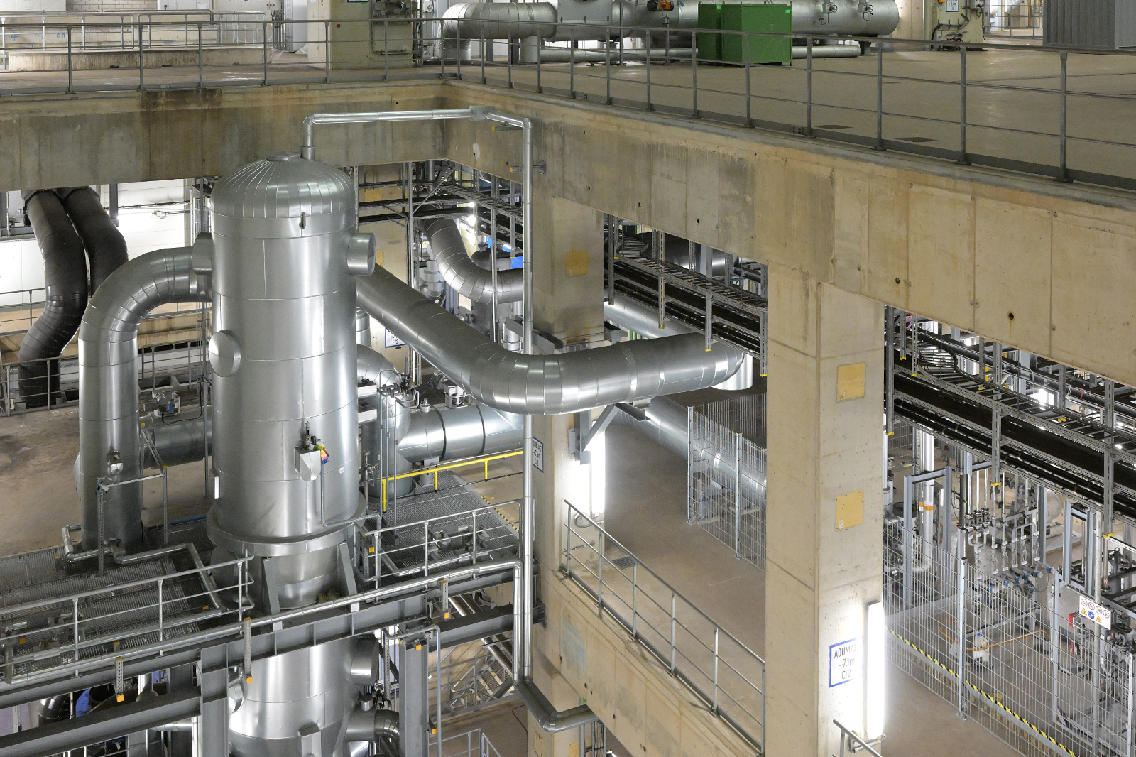 An industrial facility featuring large metallic pipes and a storage unit, illuminated by bright lights from above.