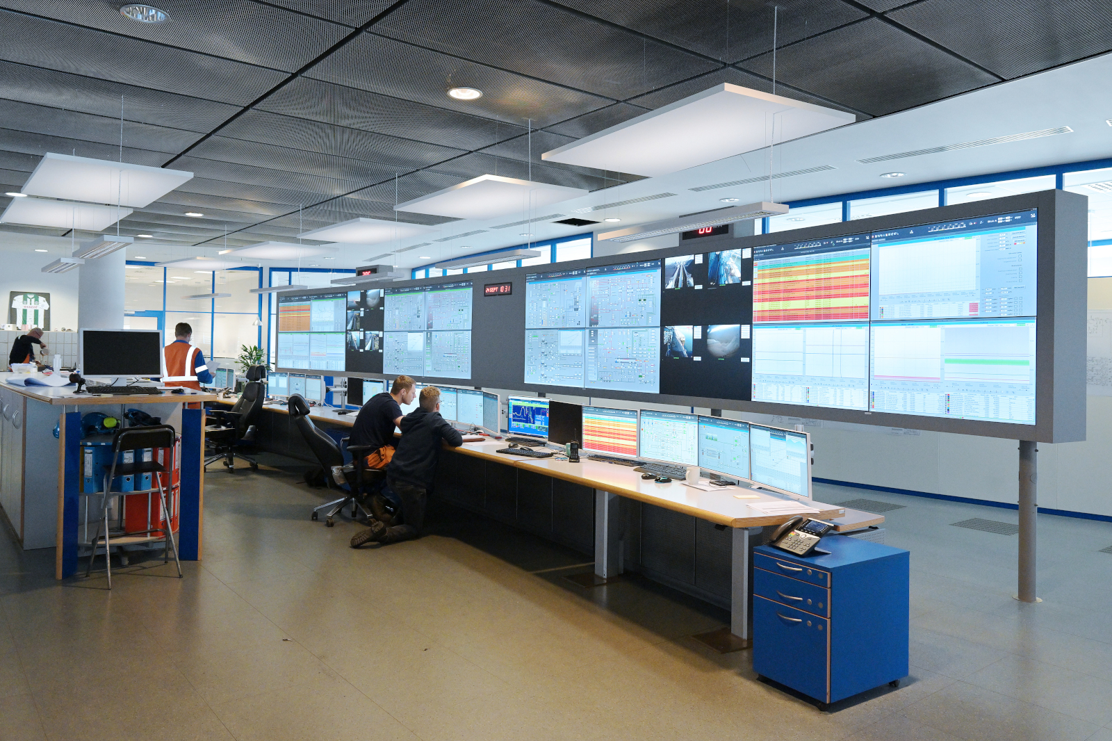 A modern control room with multiple screens displaying data, where two operators are working intently.