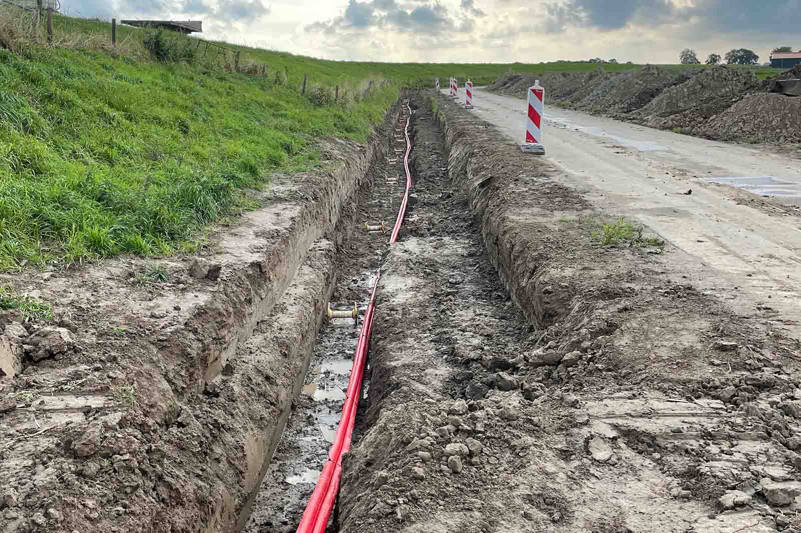 Long roadside trench containing red utility conduits and traffic bollards