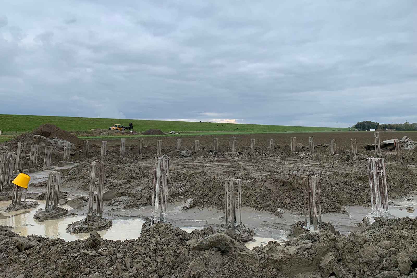 Modderige bouwplaats met betonnen grondpalen met wapeningskooien en gele helm
