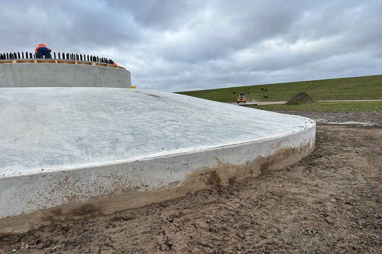 Circular concrete foundation on muddy field with worker and rebar