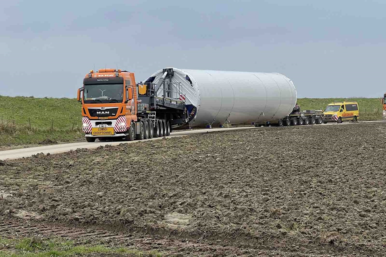 Orange heavy truck with 'MAN' logo hauling white turbine tower section