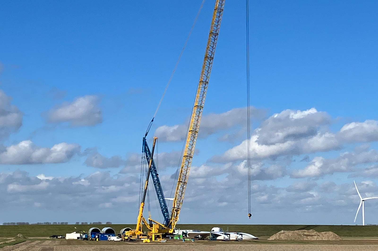 Yellow crawler crane and blue crane lifting wind turbine blade sections
