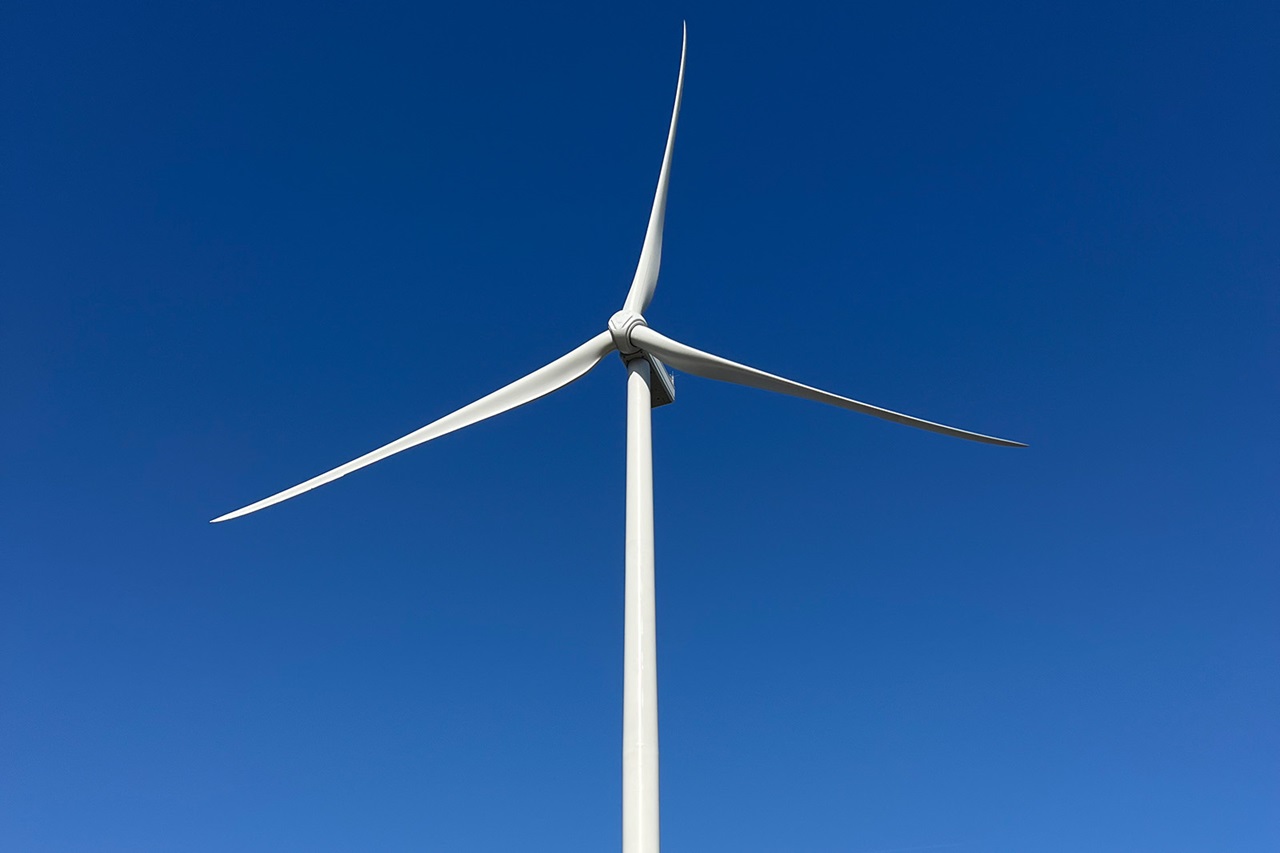 Witte windturbine met drie wieken tegen blauwe lucht
