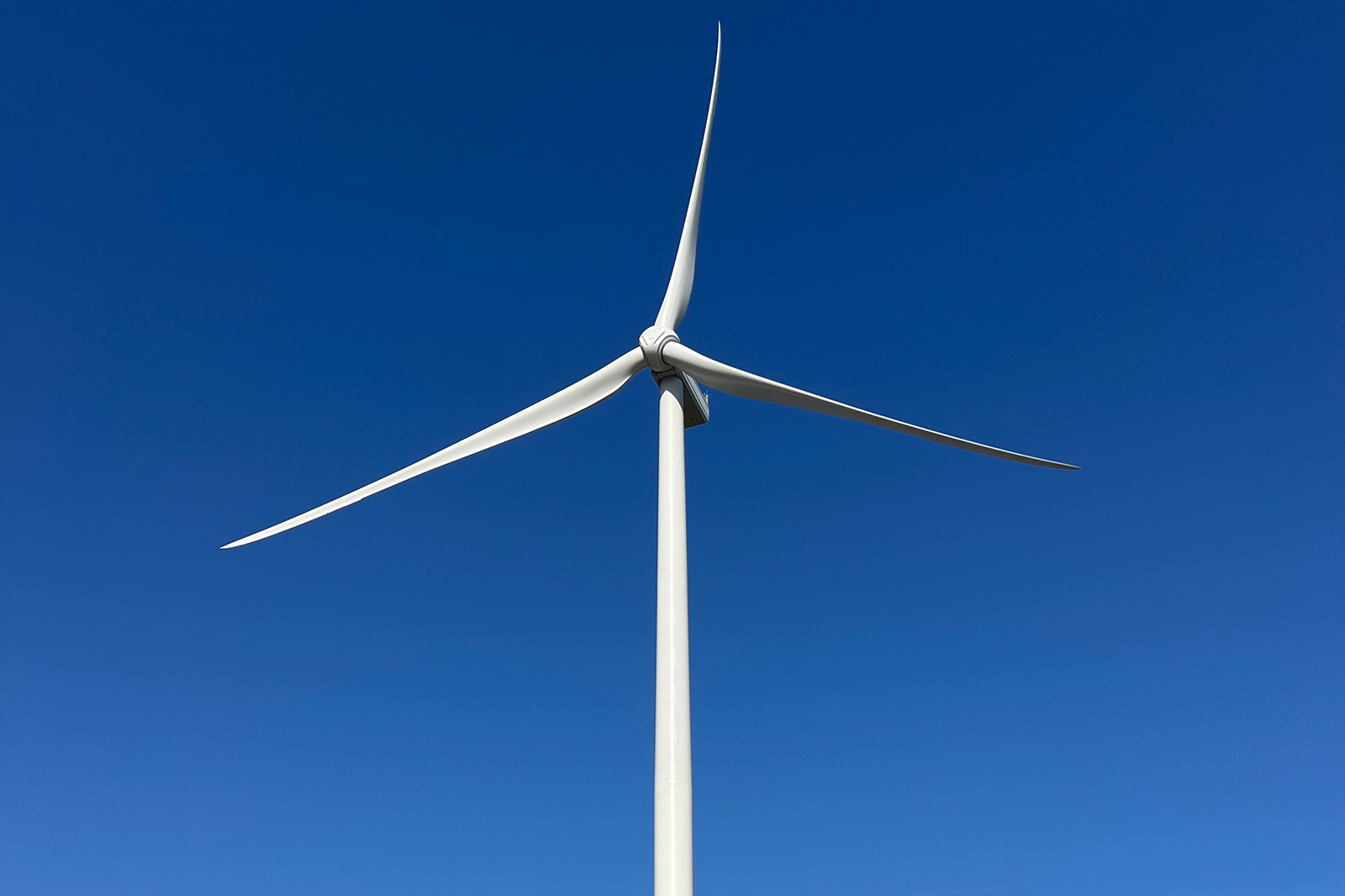 White wind turbine tower and three blades against blue sky