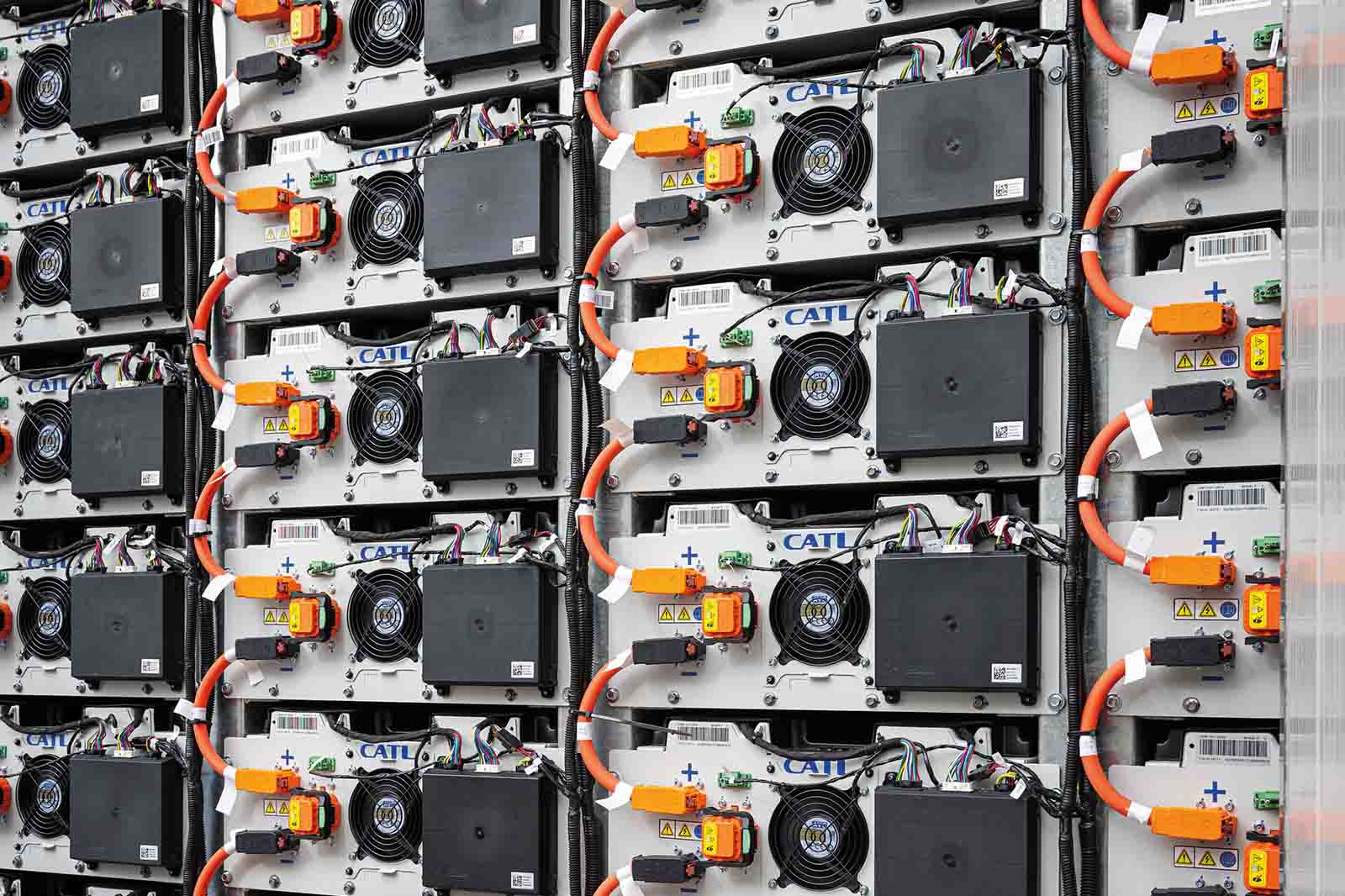 A close-up view of stacked industrial battery modules with metal casings, black cooling fans and bright orange high-voltage cables, each labeled "CATL" on white panels.