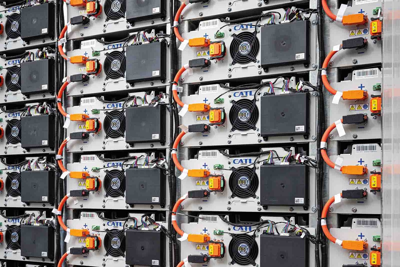 Close-up weergave van gestapelde industriële batterijmodules met metalen kasten, zwarte koelventilatoren en feloranje hoogspanningskabels, elk gemarkeerd met "CATL" op witte panelen.