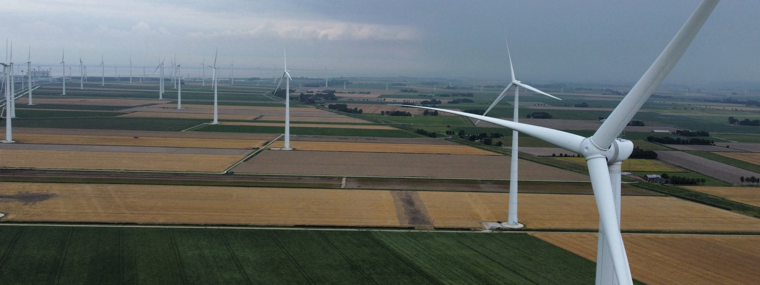 Aerial view of a wind farm with multiple turbines set against a cloudy sky and expansive farmland.
