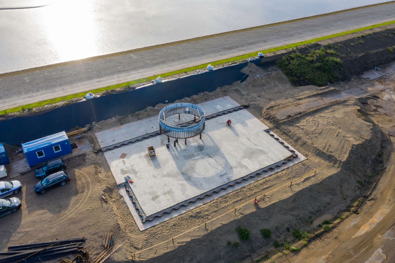 Een luchtfoto van een bouwplaats met een ronde structuur in het midden en geparkeerde voertuigen in de buurt.