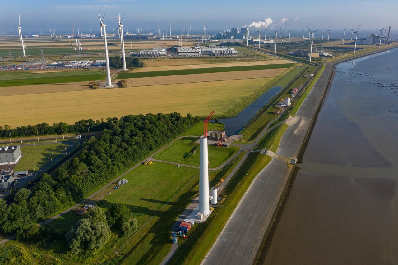 Luchtfoto van windturbines en een groen landschap, met een windpark langs water en akkers.