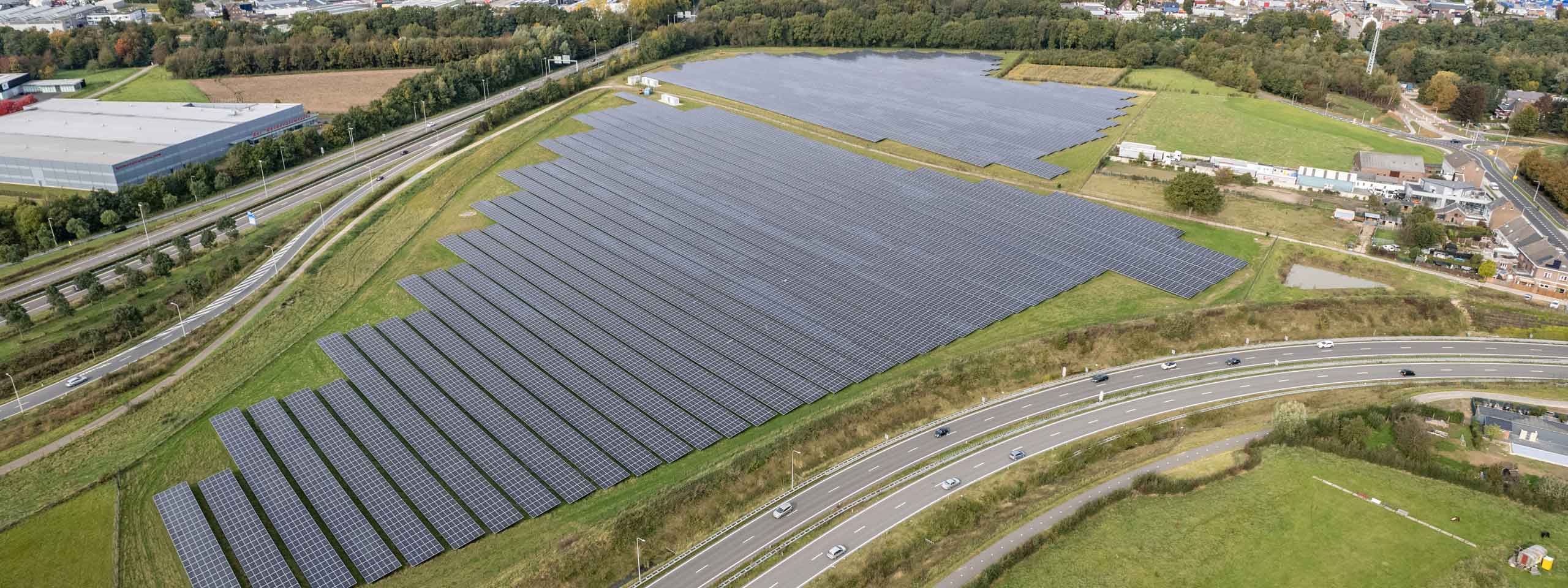 An aerial view of a solar farm with vast solar panels, alongside a winding road and green fields.