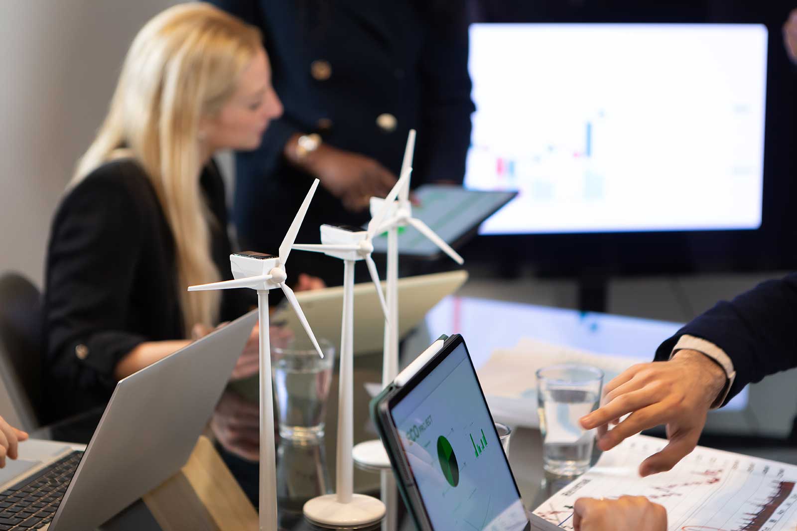Vergadering in een modern kantoor met modellen van windturbines op de tafel en laptops met grafieken en gegevens.