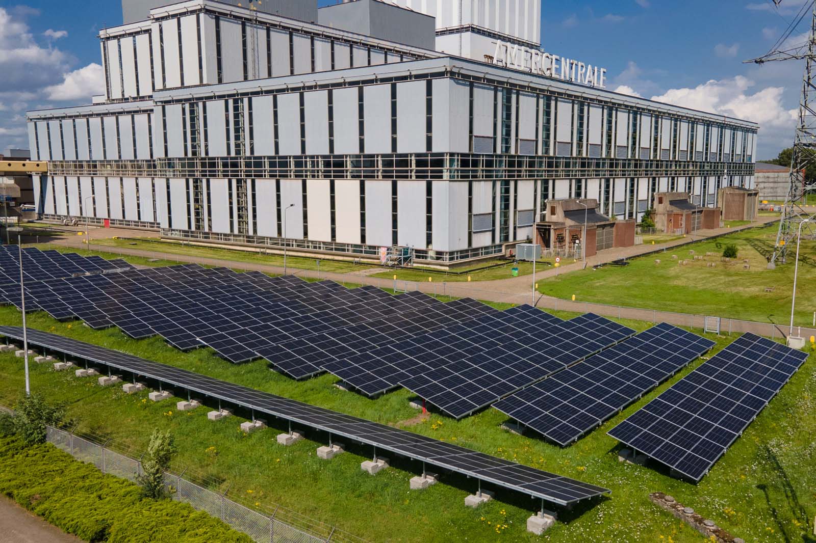 Luchtfoto van zonnepanelen voor een groot industrieel gebouw, met een heldere lucht erboven.