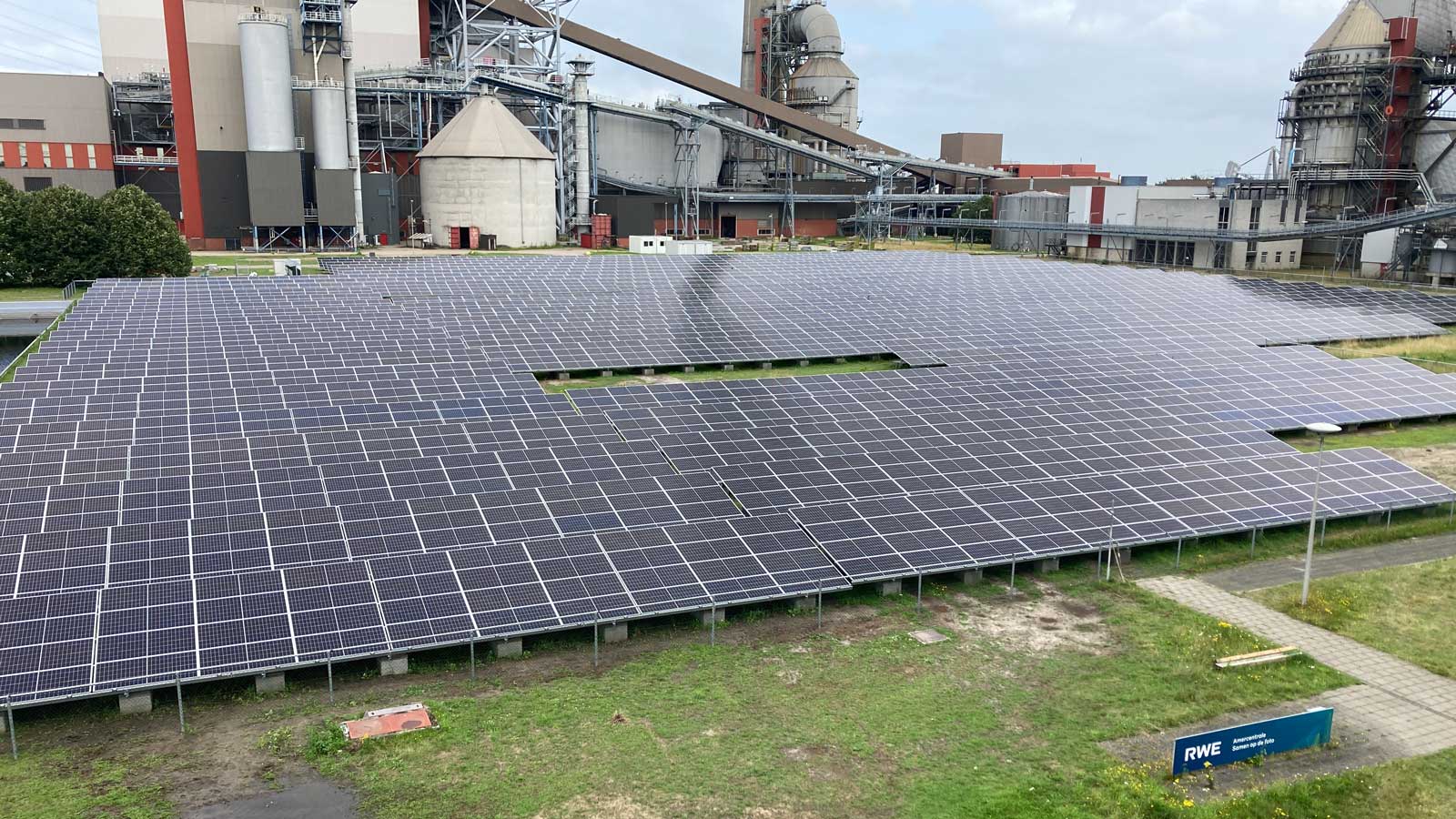 Een zonnepanelenveld met meerdere zonnepanelen voor een industriële locatie, onder een bewolkte lucht.