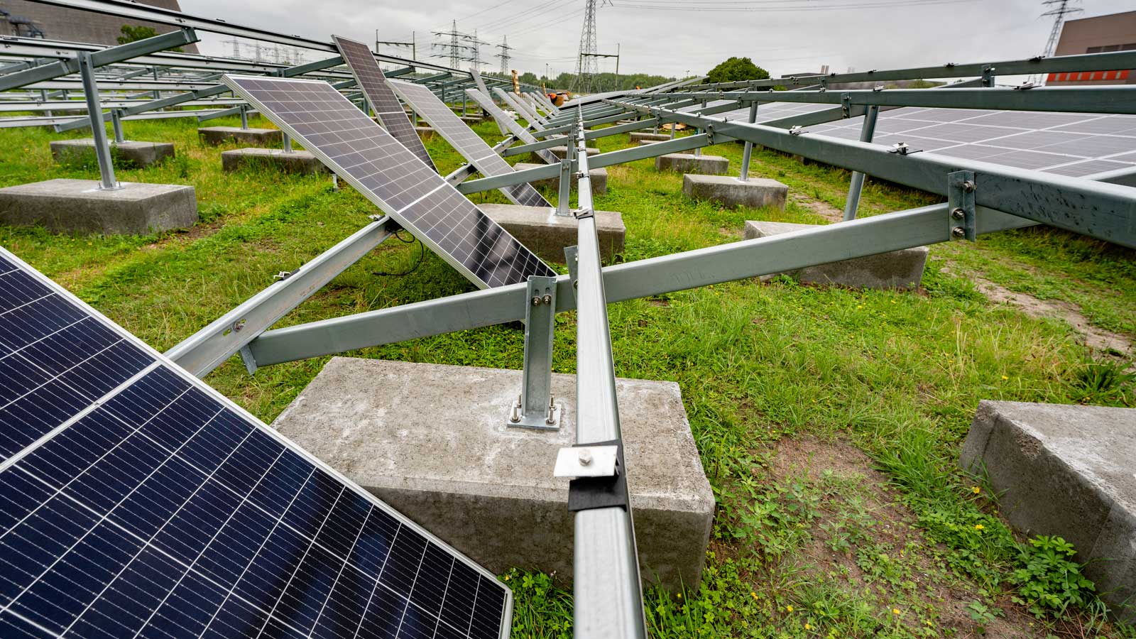 Een zonnepaneelinstallatie met meerdere panelen onder een hoek, gelegen op een grasveld met betonnen ondersteuningen.
