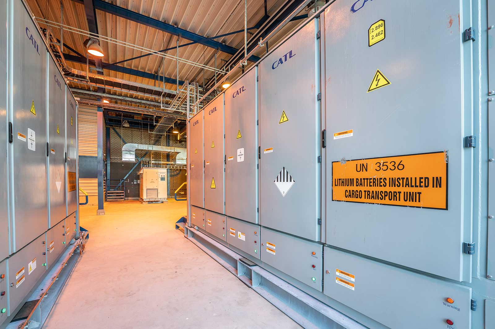 Een industriële ruimte met grijze kasten gemarkeerd met waarschuwingsborden, die lithiumbatterijen in een cargotransporteenheid opslaan.