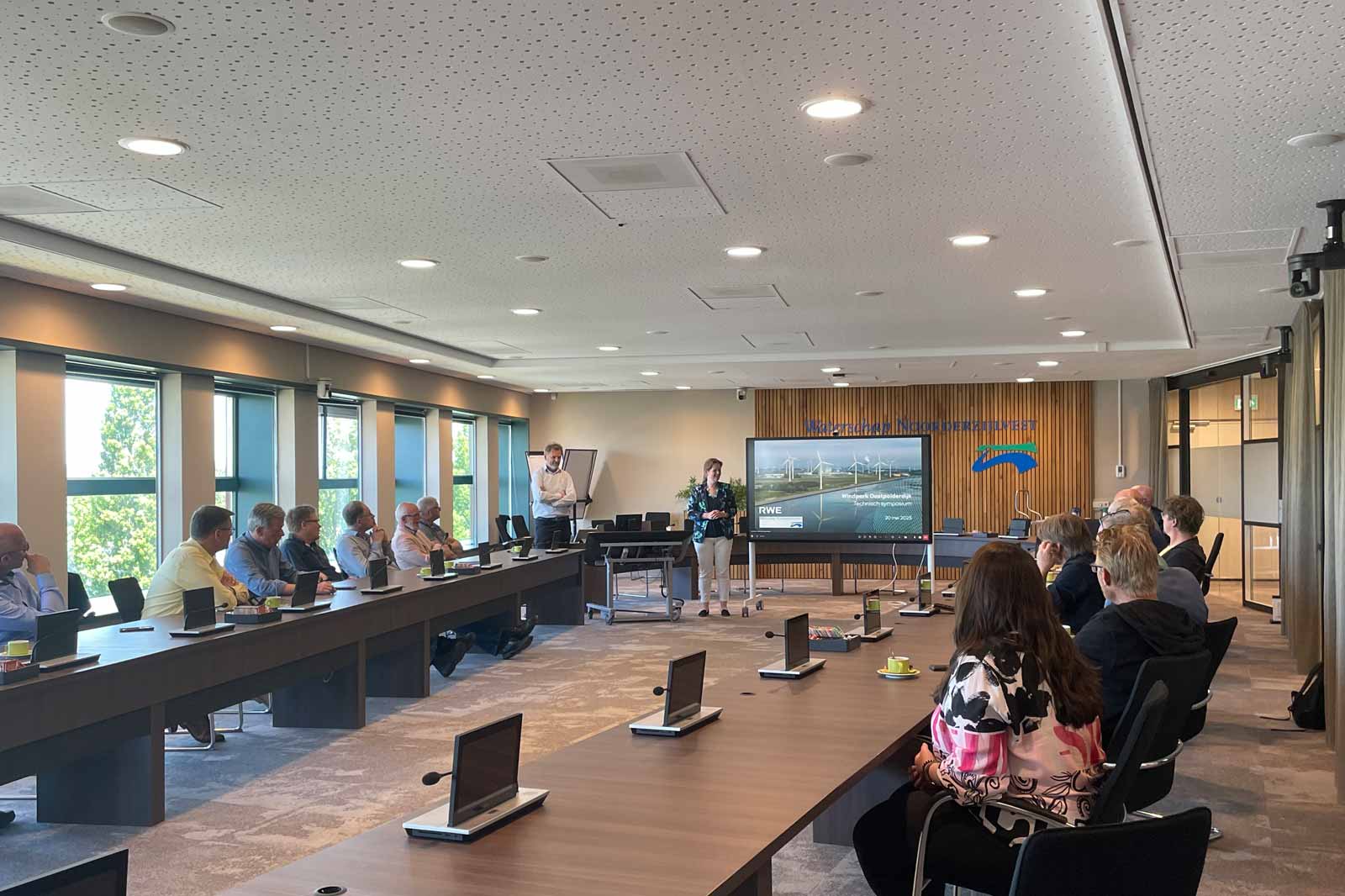 A business meeting in a modern conference room with a presenter and an audience engaged in a discussion about renewable energy.