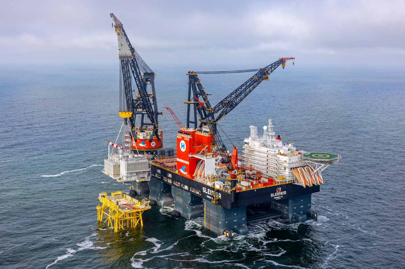 Een offshore kraanschip genaamd Sleipnir, met twee grote kranen en een gele installatieplatform in de oceaan.