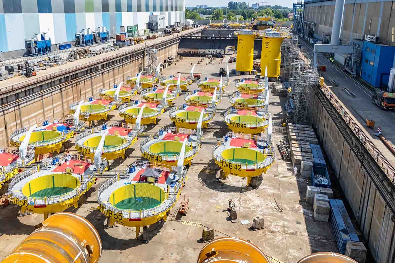 Rijen gele stalen ronde drijflichamen met groene binnenbekleding en rode toegangsdeksels op een betonnen scheepswerf, één gemarkeerd "NWB42".