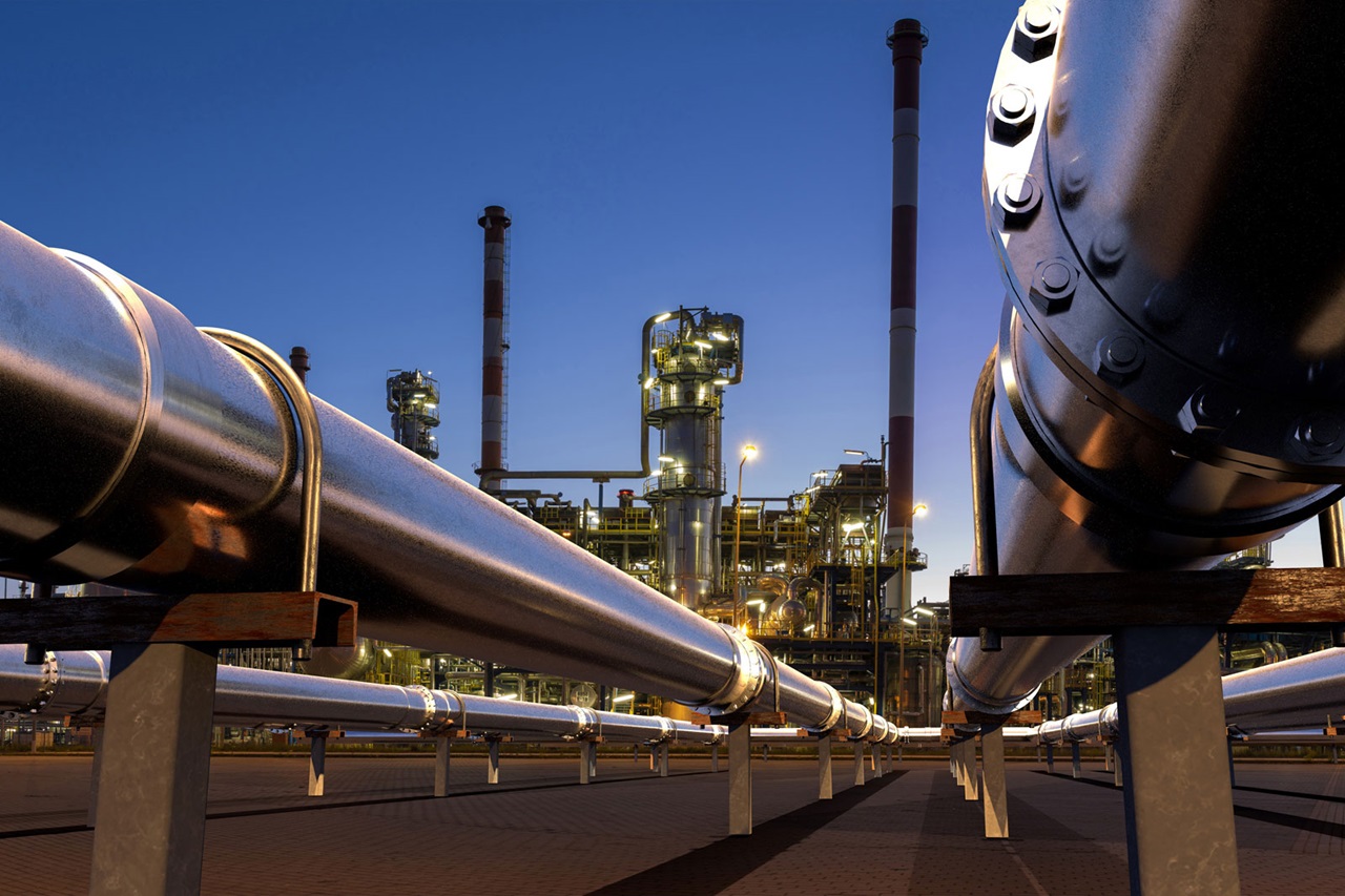 Een industrieel landschap met grote metalen pijpleidingen en een raffinaderijstructuur tegen een schemerige lucht.