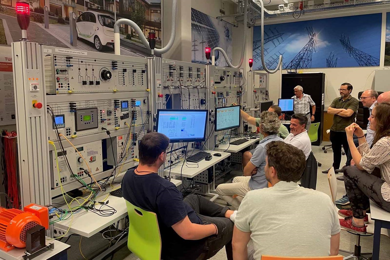 A group of people working with multiple computer monitors and control panels in a technical lab environment.