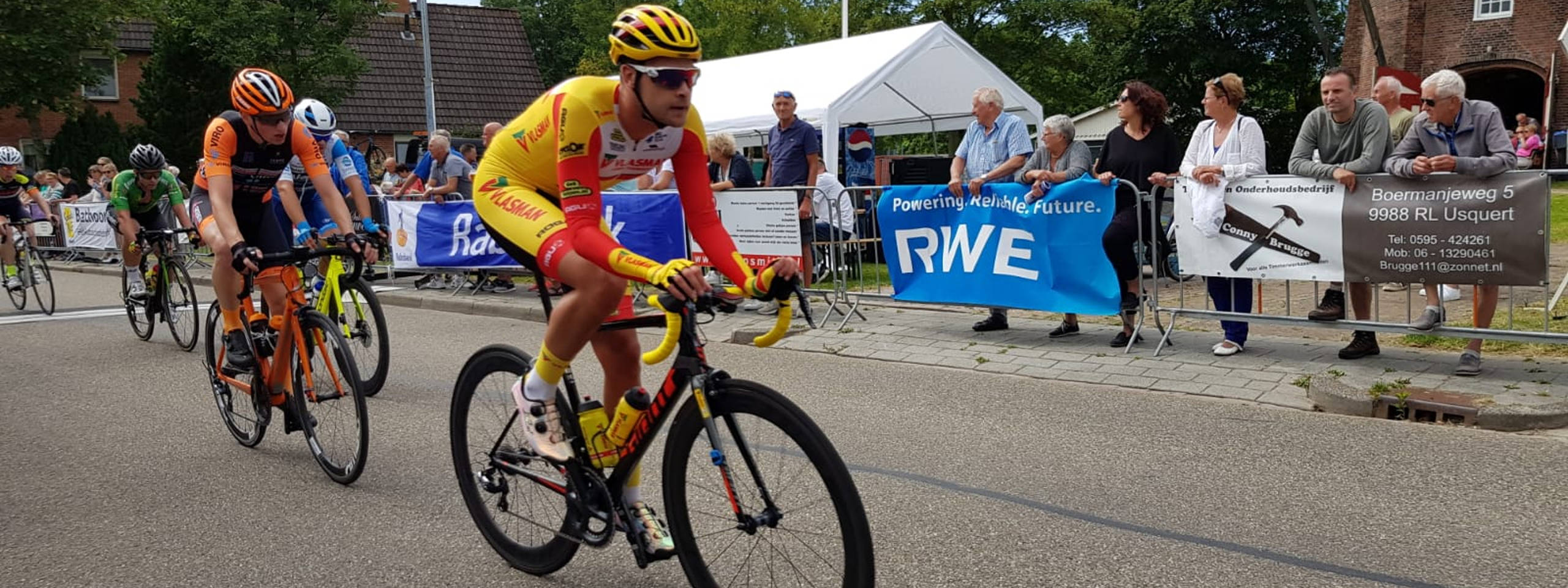 Fietsers concurreren op een weg met toeschouwers en spandoeken op de achtergrond tijdens een fiets evenement.