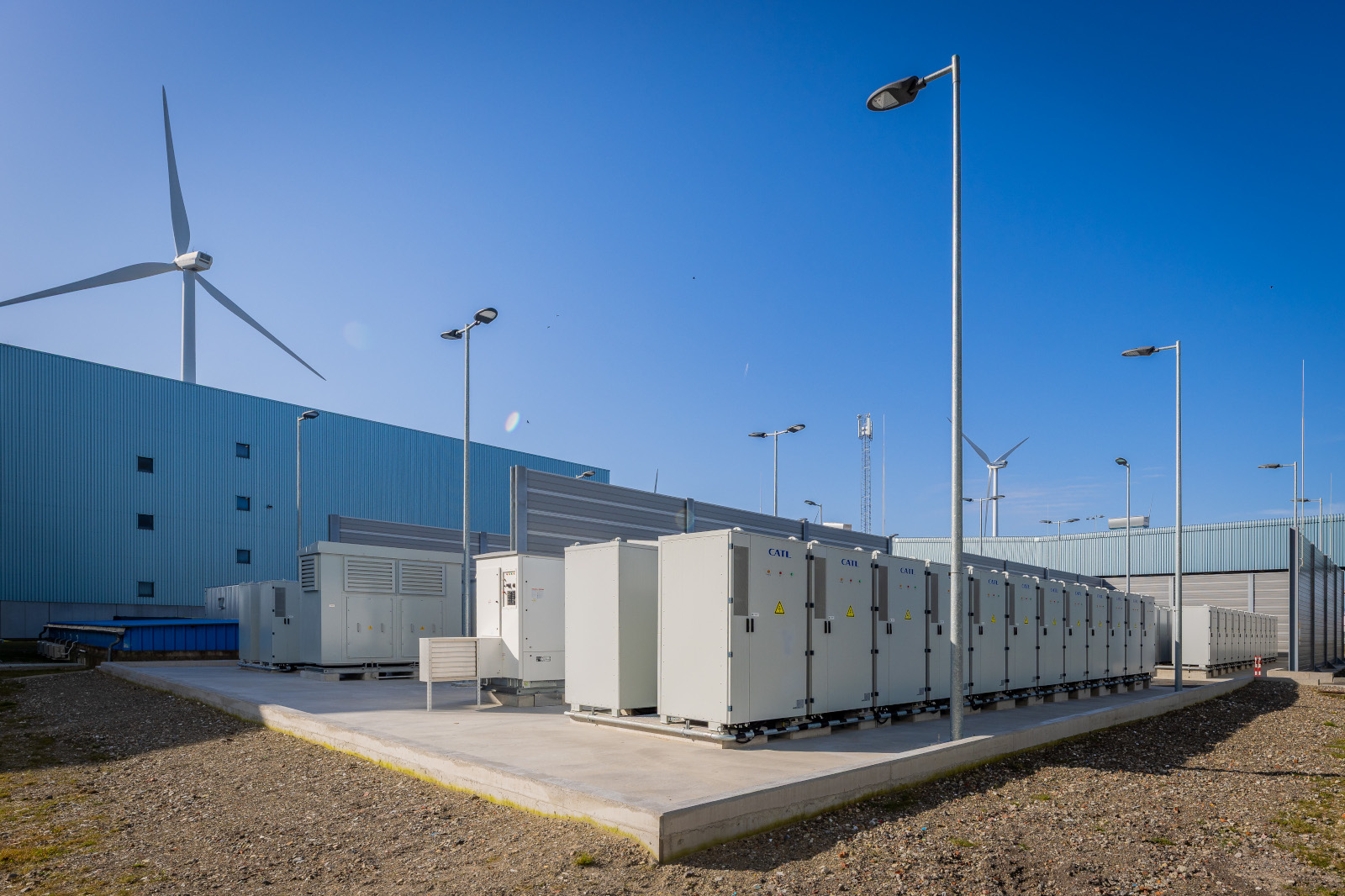 A large-scale battery energy storage system, wind turbines and clear blue skies in the background.