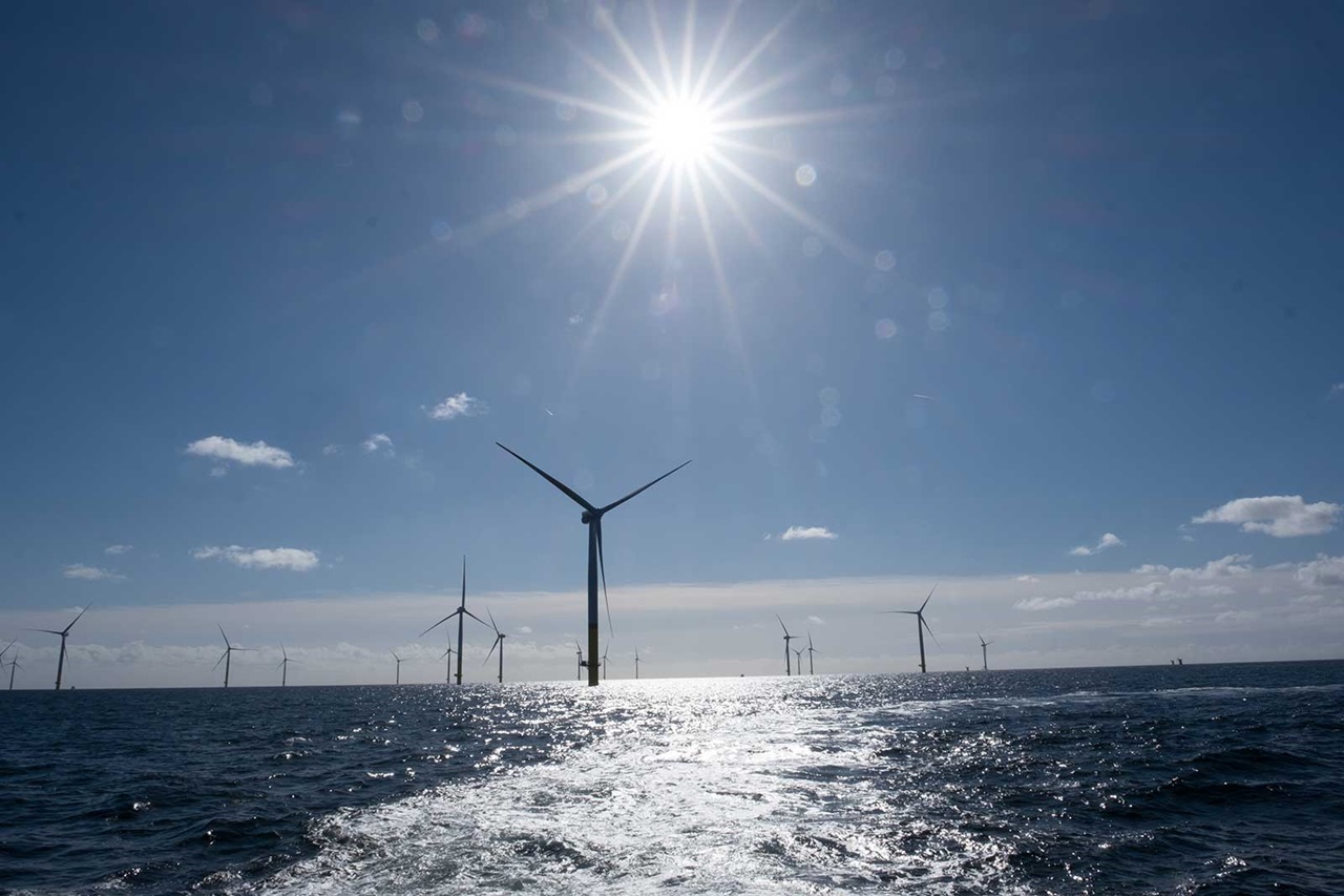 A clear sky over a sea with multiple wind turbines, reflecting sunlight and gentle waves.